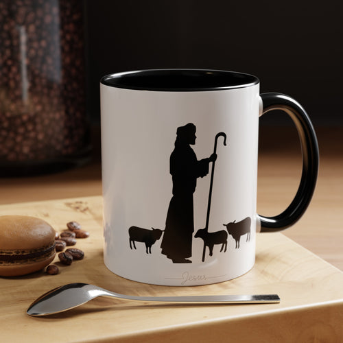 Front of the White Mug with Black Interior on Wood Table: "White ceramic coffee mug with black interior featuring a minimalist black ink design of Jesus with sheep. Displayed on a rustic wood table, this 11oz or 15oz mug is perfect for adding spiritual inspiration to your morning routine."