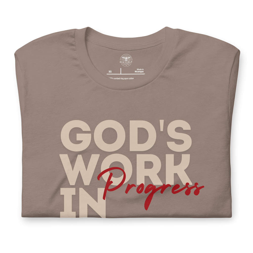 Folded Tan T-shirt by Heavenly Crafted with 'God's Work in Progress' in bold text. A soft, comfortable tee offering a daily reminder of personal growth and God's plan, inspired by Philippians 1:6.