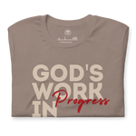 Folded Tan T-shirt by Heavenly Crafted with 'God's Work in Progress' in bold text. A soft, comfortable tee offering a daily reminder of personal growth and God's plan, inspired by Philippians 1:6.