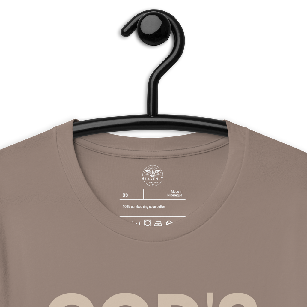 Heavenly Crafted's 'God's Work in Progress' T-shirt in Tan hanging on a black hanger, showcasing the simple yet profound design. Perfect for those who embrace their spiritual journey.