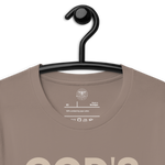 Heavenly Crafted's 'God's Work in Progress' T-shirt in Tan hanging on a black hanger, showcasing the simple yet profound design. Perfect for those who embrace their spiritual journey.