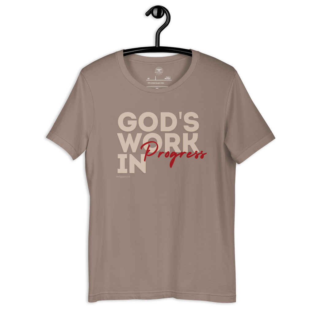 Brand and care instructions label inside Heavenly Crafted's 'God's Work in Progress' T-shirt in Tan. Hangs on a black hanger. Displays high-quality fabric details and care guidelines to maintain this soft, durable tee.