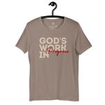 Brand and care instructions label inside Heavenly Crafted's 'God's Work in Progress' T-shirt in Tan. Hangs on a black hanger. Displays high-quality fabric details and care guidelines to maintain this soft, durable tee.