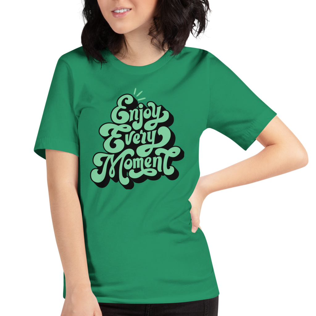 Model wearing 'Enjoy Every Moment' T-shirt in vibrant green, three-quarter view. Features bold graffiti-style lettering and a comfortable, flattering fit.