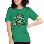 Model wearing 'Enjoy Every Moment' T-shirt in vibrant green, three-quarter view. Features bold graffiti-style lettering and a comfortable, flattering fit.