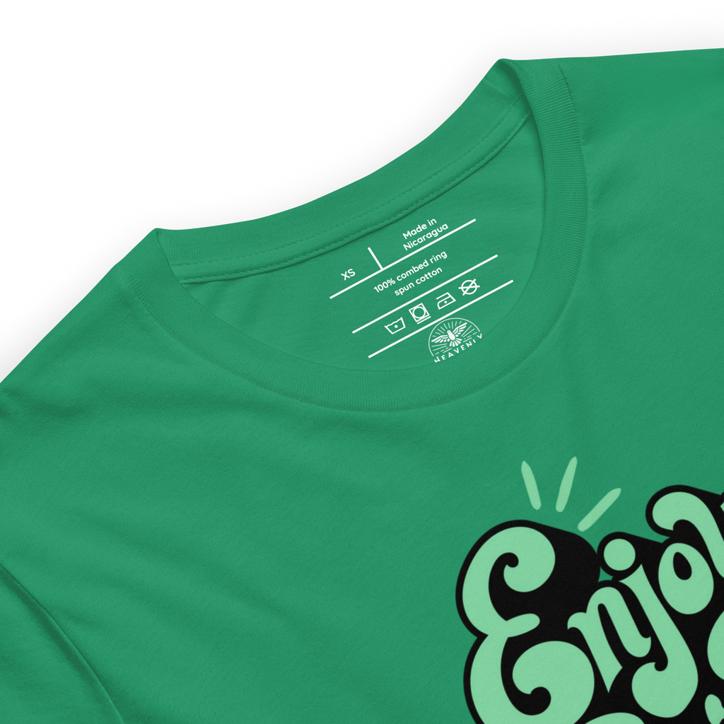 Folded green T-shirt with 'Enjoy Every Moment' in graffiti script, showcasing the vibrant design and soft, quality fabric perfect for daily wear and inspiration.