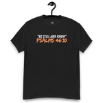 Front view of the black 'Be Still and Know' T-shirt on a wooden hanger, featuring Psalm 46:10. This faith-inspired tee offers a calming design, perfect for daily wear, encouraging peace and reflection. Crafted for comfort and style, it's an ideal addition to any spiritual wardrobe.