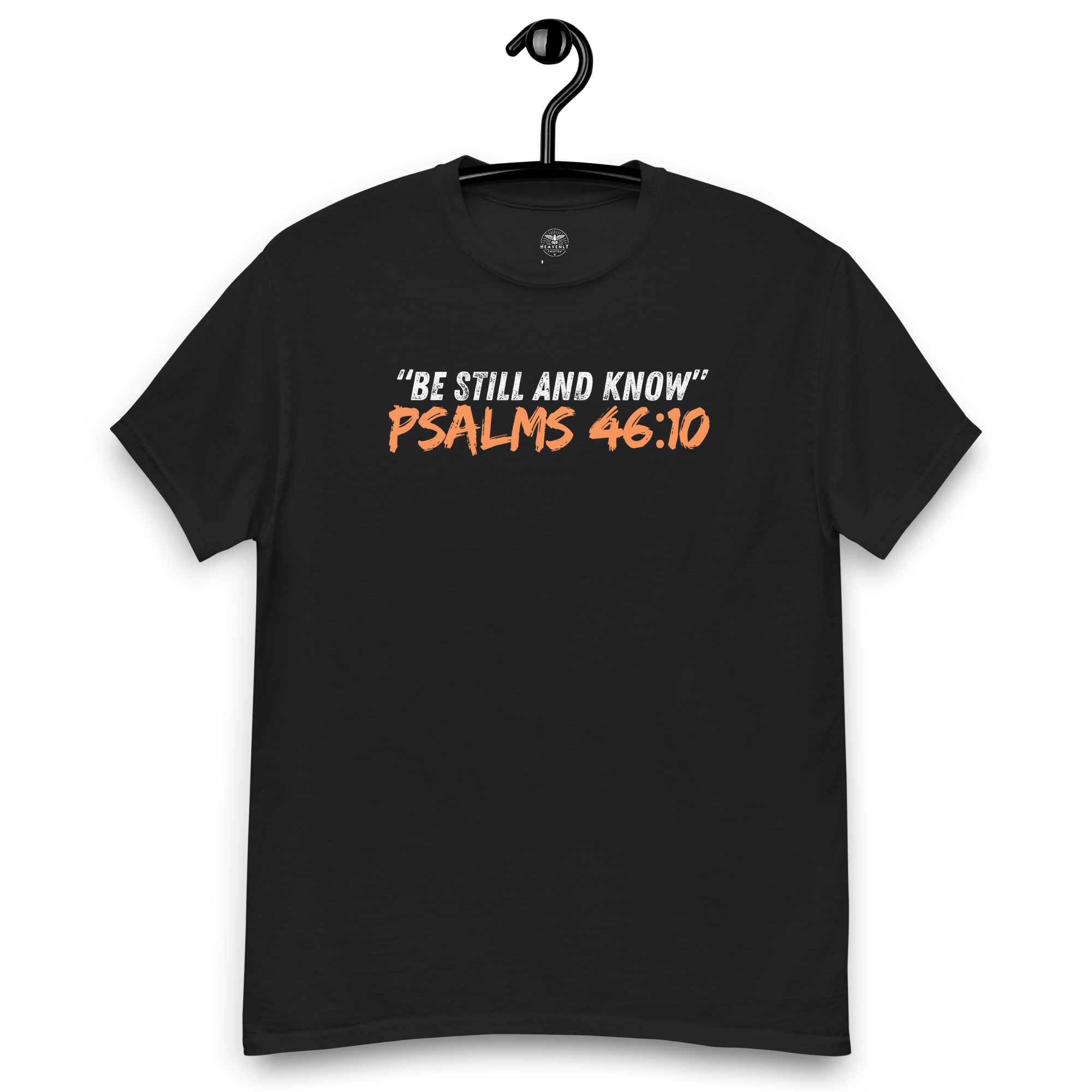 Front view of the black 'Be Still and Know' T-shirt on a wooden hanger, featuring Psalm 46:10. This faith-inspired tee offers a calming design, perfect for daily wear, encouraging peace and reflection. Crafted for comfort and style, it's an ideal addition to any spiritual wardrobe.