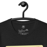 Logo stamp inside the 'Let Your Light Shine' T-shirt in Black Heather, displayed on a hanger, showing brand details and care instructions. Highlights the high-quality, durable construction of this faith-inspired garment.