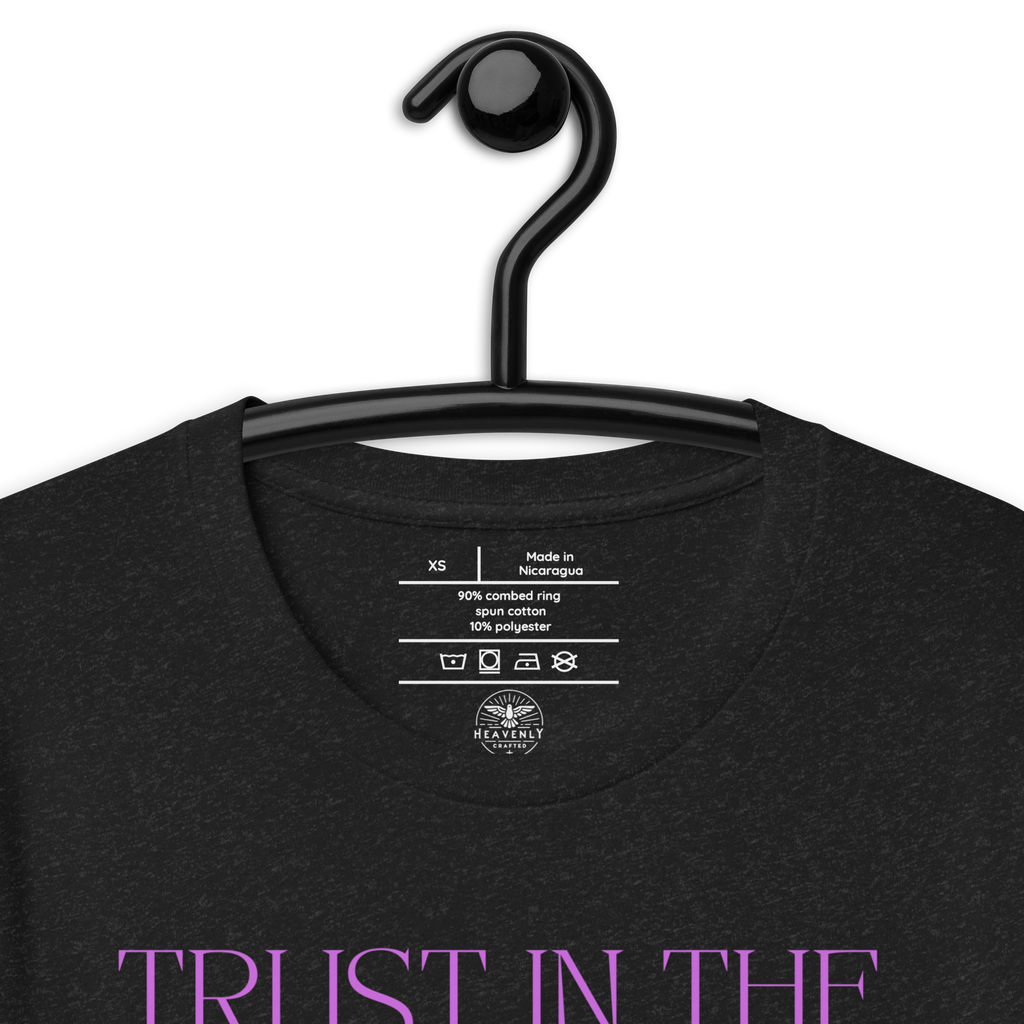 Logo stamp inside 'Trust in the Lord' T-shirt in Black Heather, showing brand and care instructions, on a hanger.