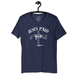 Black 'Jesus Paid It All' T-shirt hanging on a wooden hanger.