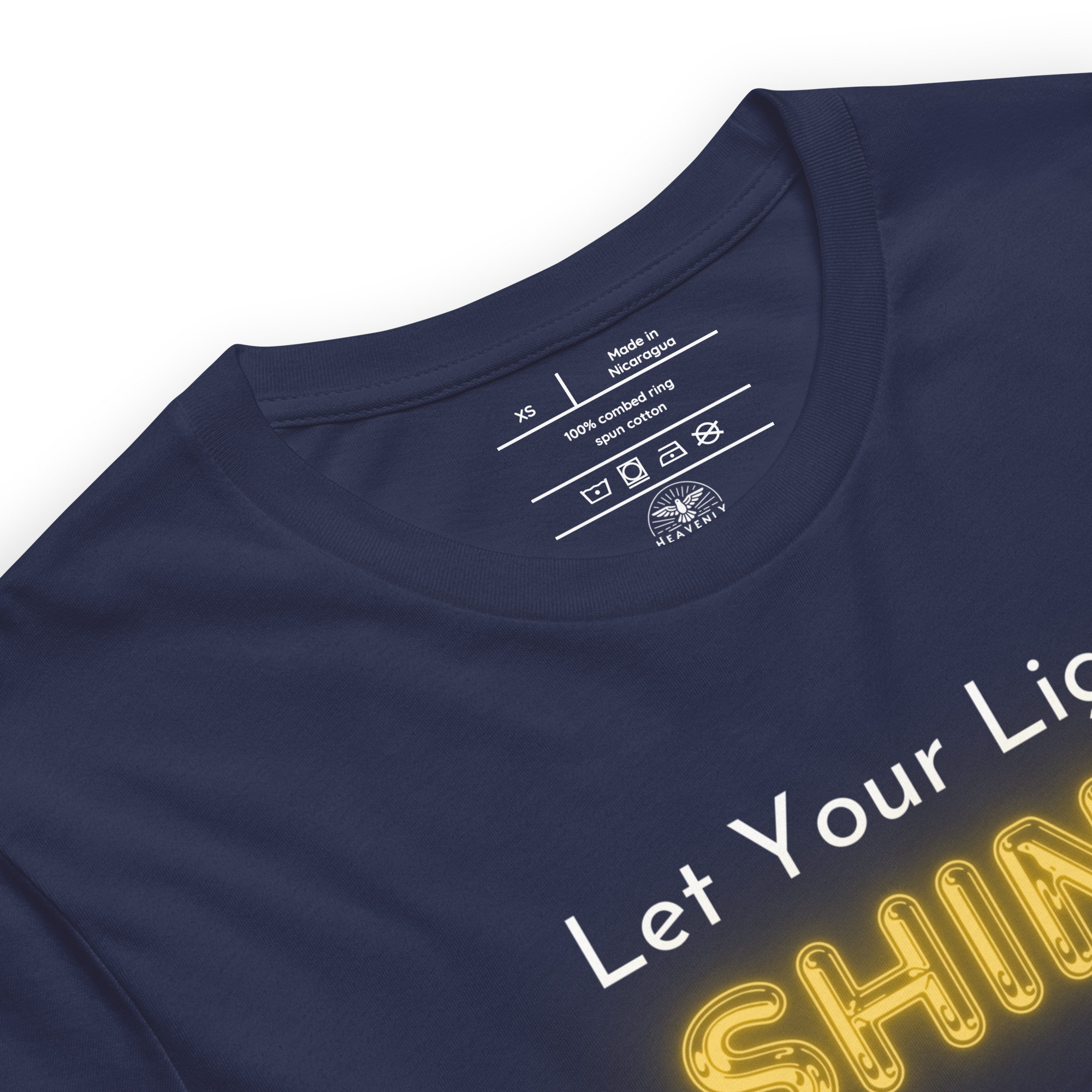 Logo stamp inside 'Let Your Light Shine' T-shirt in navy, showing brand and care instructions. Heavenly Crafted