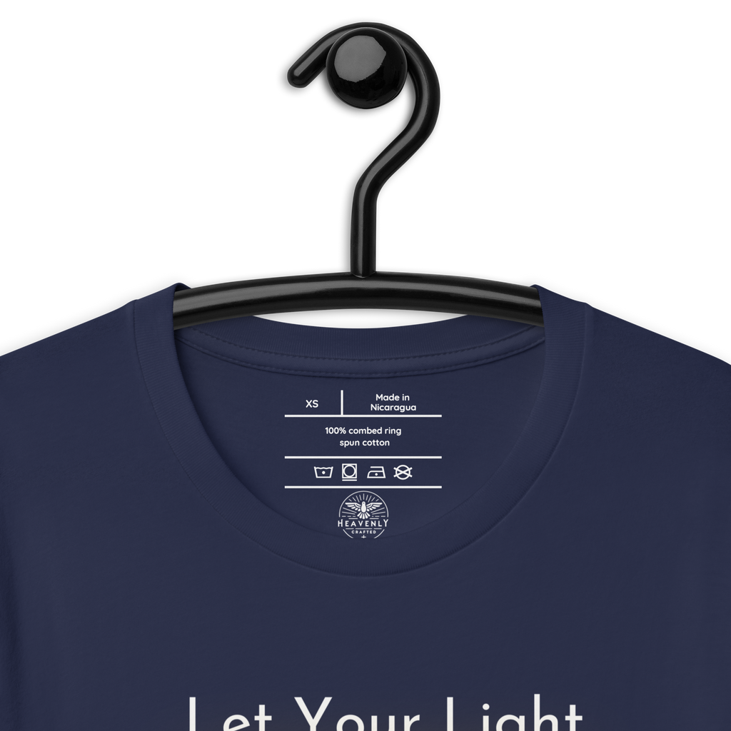 Logo stamp inside 'Let Your Light Shine' T-shirt in navy, showing brand and care instructions on a hanger