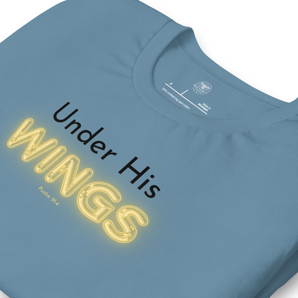 Folded navy blue T-shirt with 'Under His' in black text and 'Wings' in glowing yellow. "Logo stamp inside 'Under His Wings' T-shirt in navy blue, showing brand and care instructions.