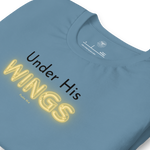 Folded navy blue T-shirt with 'Under His' in black text and 'Wings' in glowing yellow. "Logo stamp inside 'Under His Wings' T-shirt in navy blue, showing brand and care instructions.