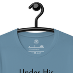 Navy blue 'Under His Wings' T-shirt hanging on a wooden hanger. Logo stamp inside 'Under His Wings' T-shirt in navy blue, showing brand and care instructions.