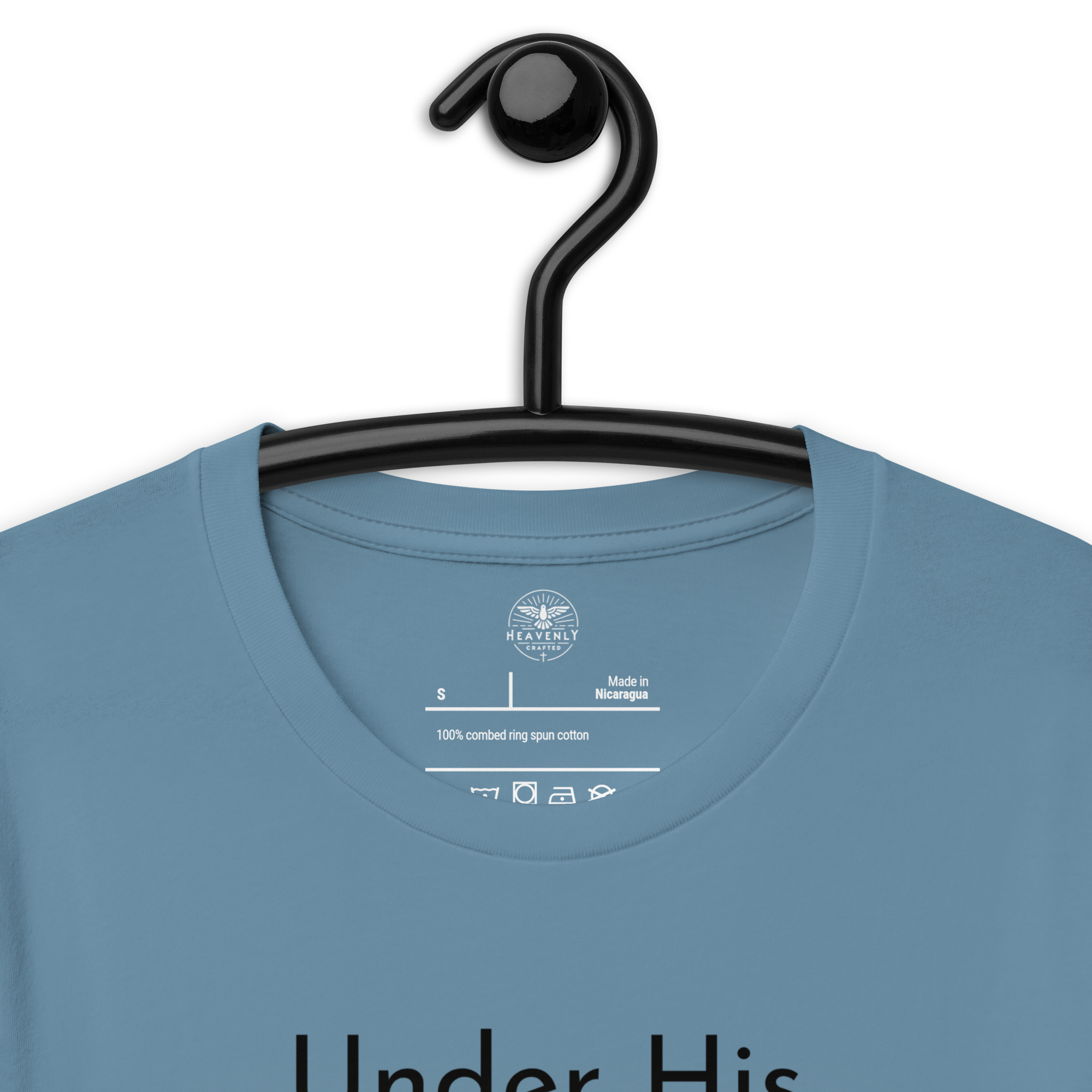 Navy blue 'Under His Wings' T-shirt hanging on a wooden hanger. Logo stamp inside 'Under His Wings' T-shirt in navy blue, showing brand and care instructions.